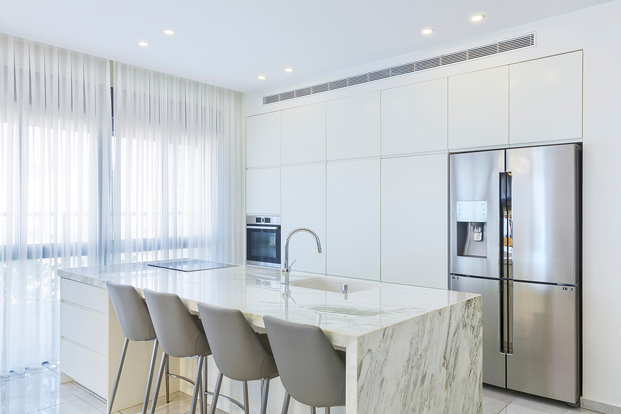 A white kitchen with an island that has a marble waterfall countertop, a sink, and four seats